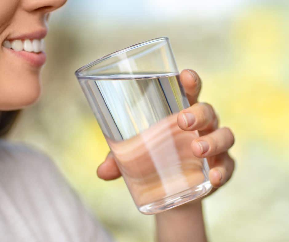 Žena pije čašu vode kao dio prevencije za zaštitu zubne cakline od erozije